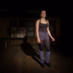 Sarah Genne as Mavis in Stagedoor Manor's production of Stepping Out, standing in dance rehearsal wear with leg warmers and tap shoes on a wooden studio floor.